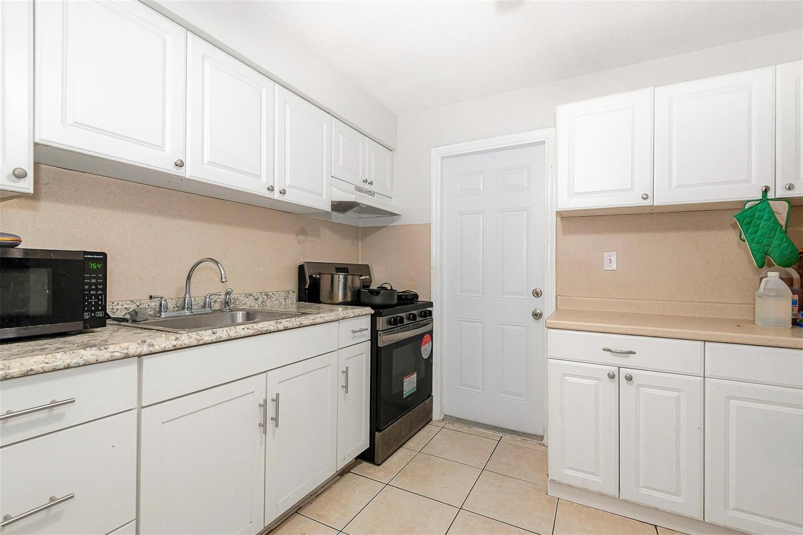 A kitchen features white cabinets, granite countertops, a stainless steel stove, and tile flooring — 404 NE 4th Street, Pompano Beach FL 33060, POMPANO BEACH, FL