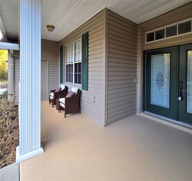 A covered front porch features tan siding, a dark green front door, and two chairs — 25344 CROOM ROAD, BROOKSVILLE, FL