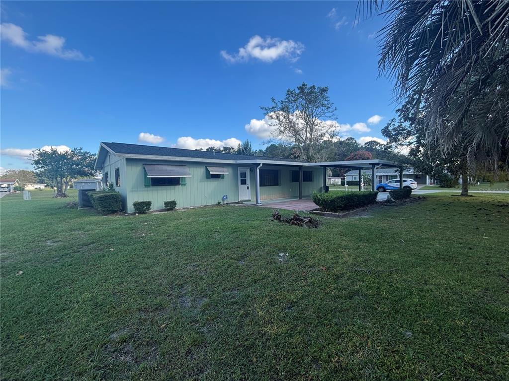 A light green single-story house features a covered patio, a carport, and a grassy yard — 10211 SW 93RD COURT, OCALA, FL