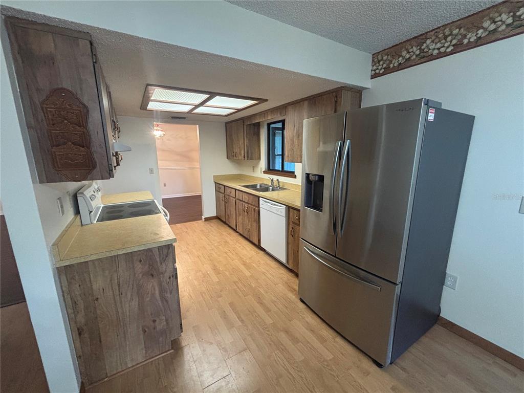 A kitchen features wood cabinets, laminate countertops, stainless steel appliances, and light wood flooring — 10211 SW 93RD COURT, OCALA, FL