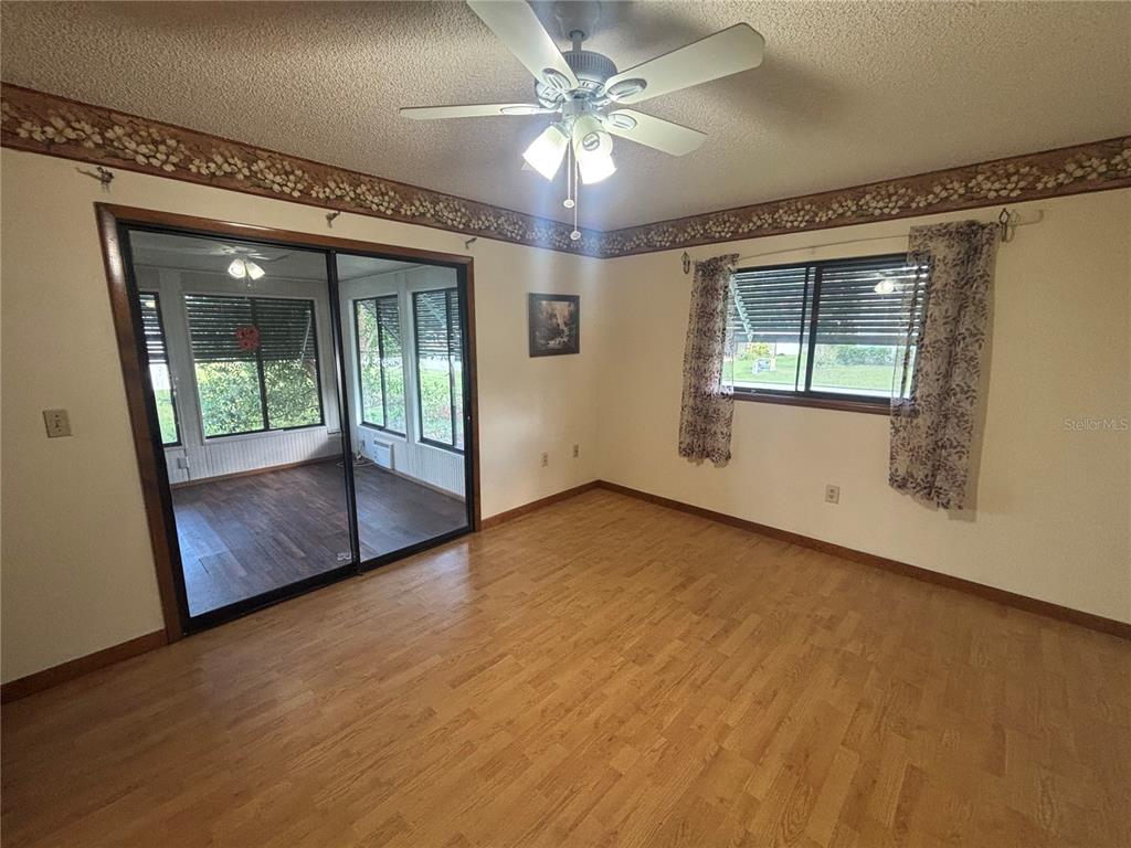 A room with light wood flooring, a ceiling fan, and sliding glass doors to a sunroom — 10211 SW 93RD COURT, OCALA, FL