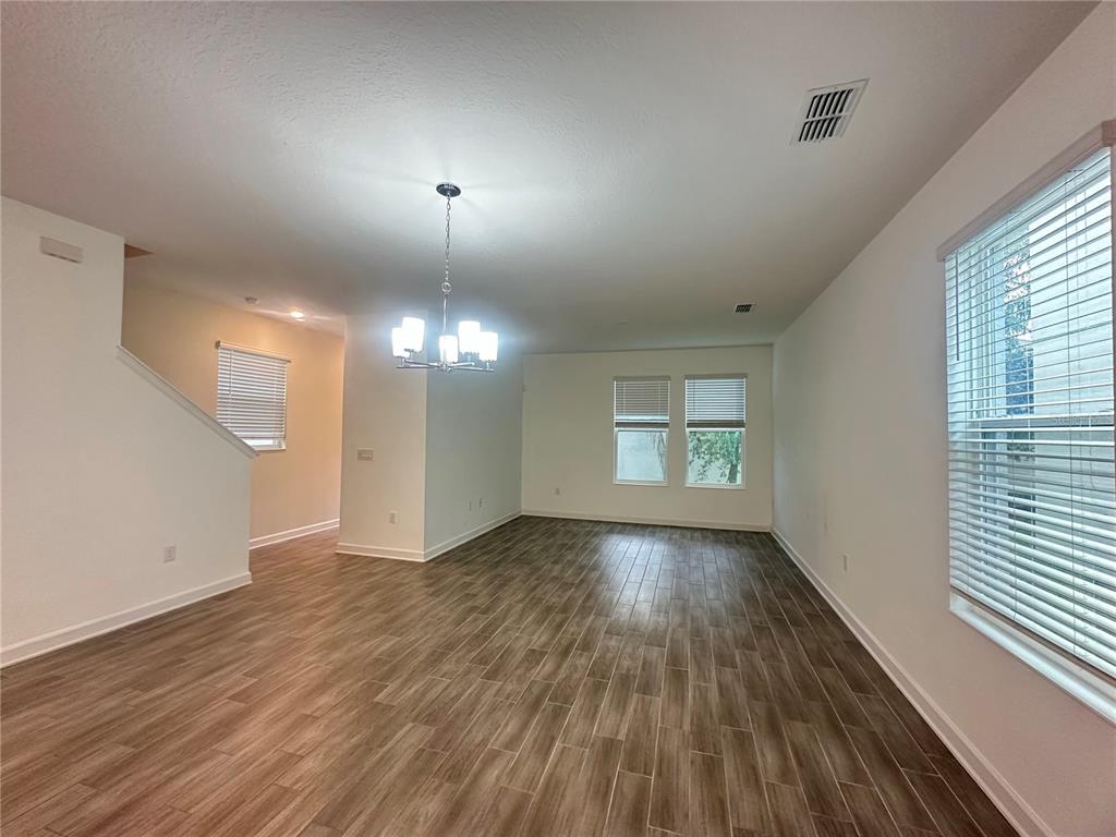 An empty room with wood-look tile flooring, a dining chandelier, and several windows with blinds — 14180 TITLE WAY, WINTER GARDEN, FL