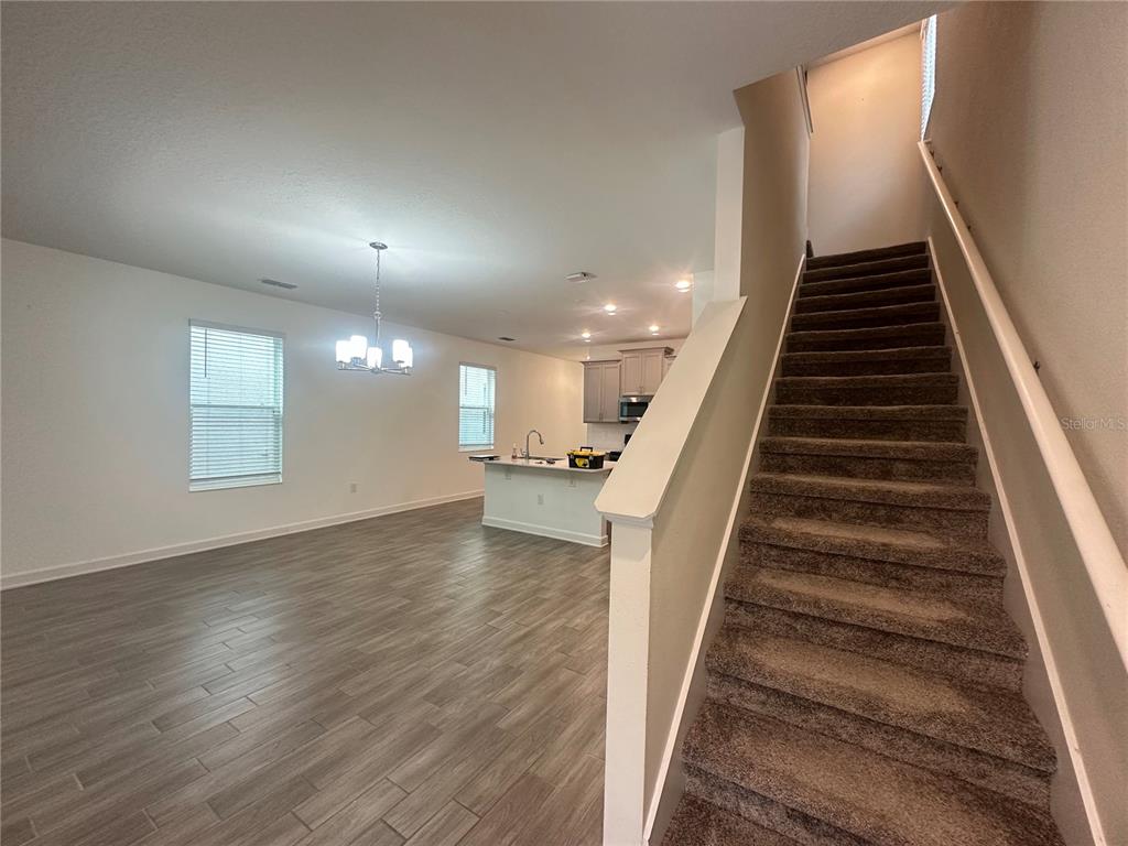 An open-concept living area features wood-look tile flooring, a kitchen island, and carpeted stairs — 14180 TITLE WAY, WINTER GARDEN, FL
