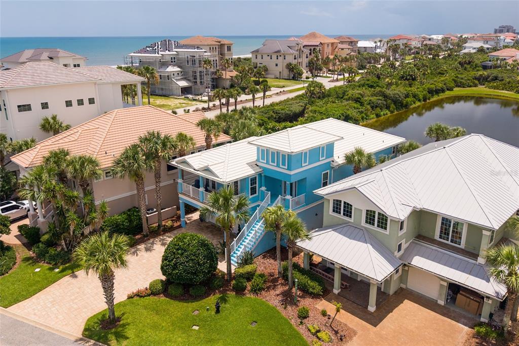 An aerial view shows three coastal houses, including a bright blue home, near a pond — 550 CINNAMON BEACH LANE, PALM COAST, FL