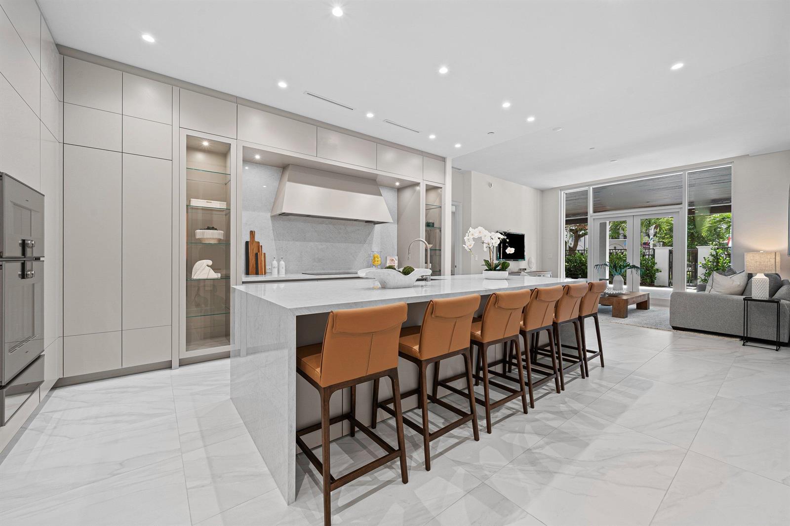 A modern kitchen features a large marble island with tan bar stools and light cabinetry — 220 SE Mizner Boulevard # 102, Boca Raton FL 33432, BOCA RATON, FL
