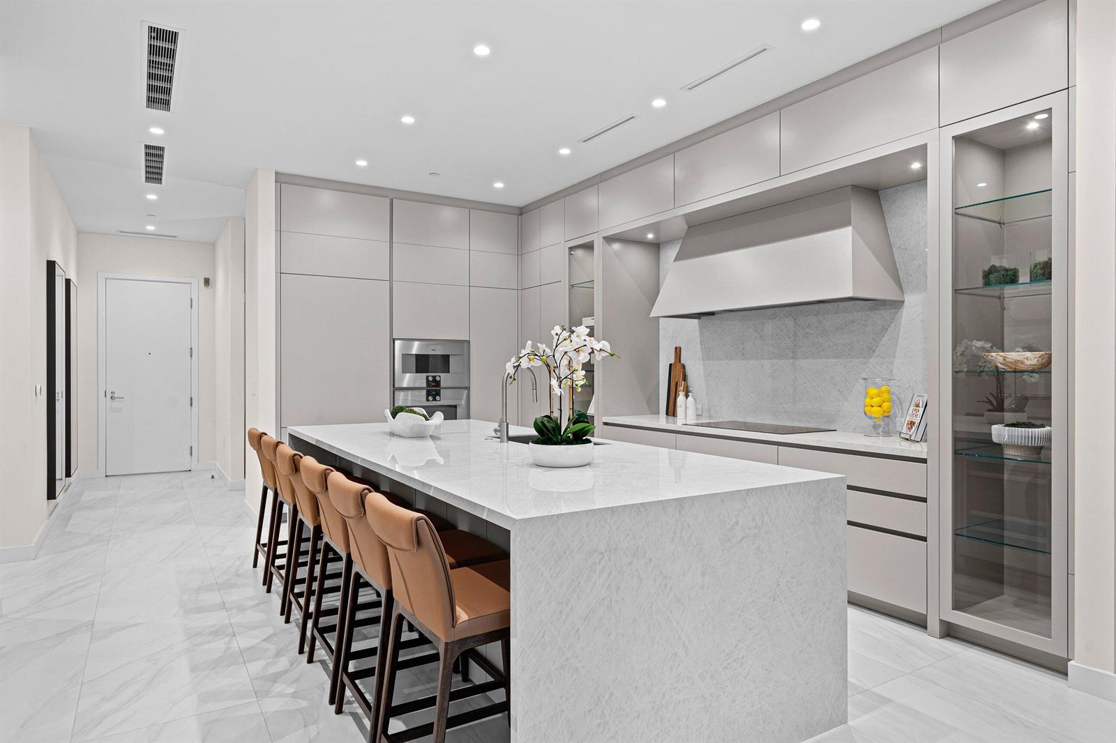 A modern kitchen features a large marble island, tan bar stools, and light gray cabinetry — 220 SE Mizner Boulevard # 102, Boca Raton FL 33432, BOCA RATON, FL