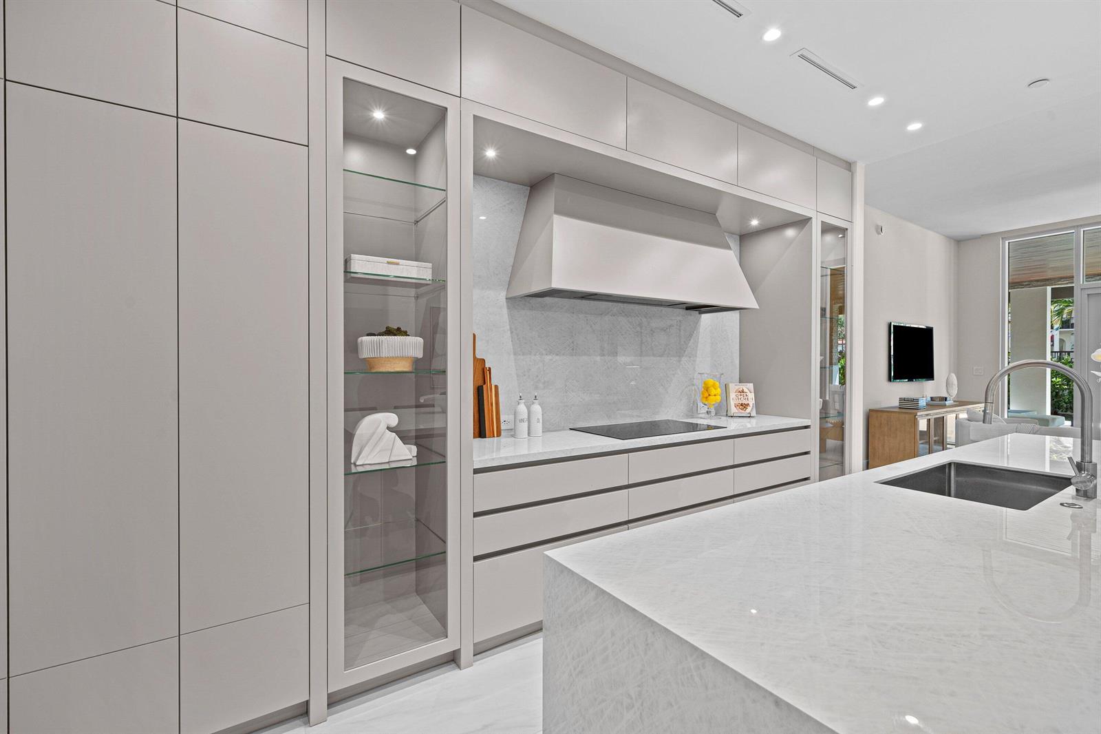 A modern kitchen features light gray cabinetry, a marble countertop, and a glass-front display cabinet — 220 SE Mizner Boulevard # 102, Boca Raton FL 33432, BOCA RATON, FL