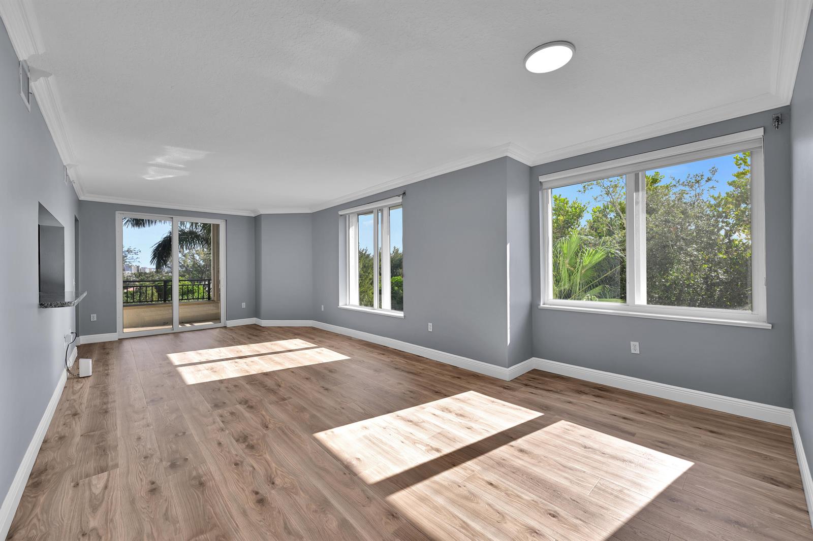 An empty living room features gray walls, light wood-look flooring, large windows, and a balcony — 2880 NE 14th St Causeway # 413, Pompano Beach FL 33062, POMPANO BEACH, FL