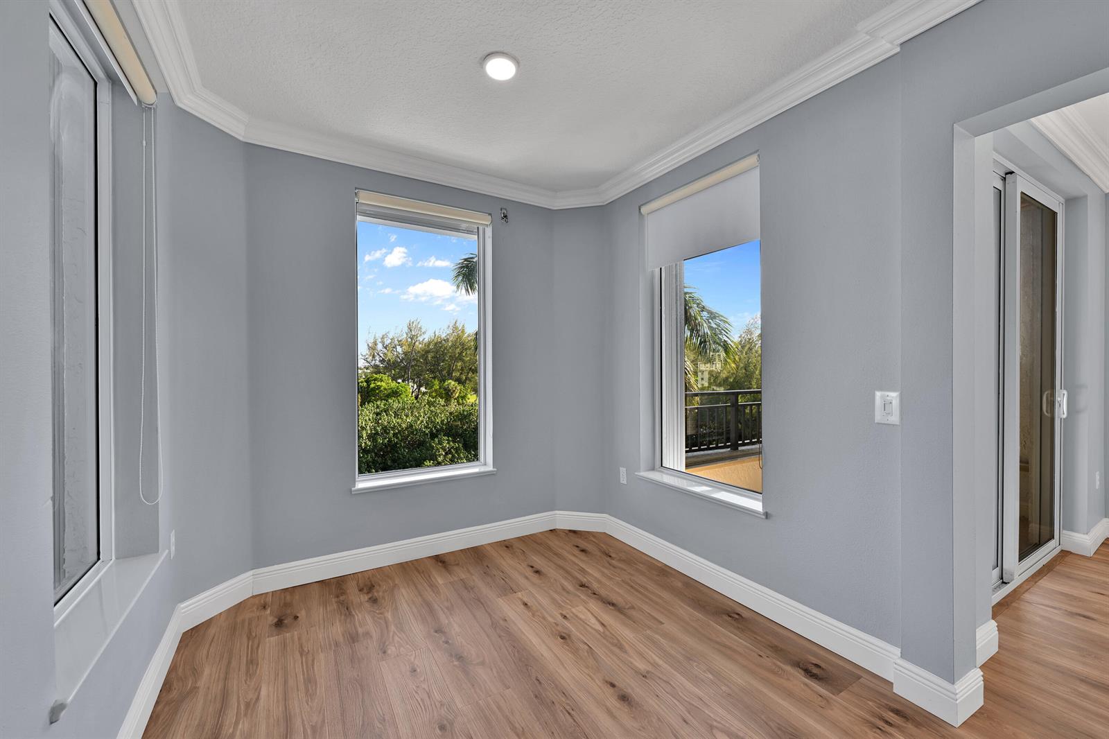 An empty room features light gray walls, wood-look flooring, and windows overlooking a balcony — 2880 NE 14th St Causeway # 413, Pompano Beach FL 33062, POMPANO BEACH, FL