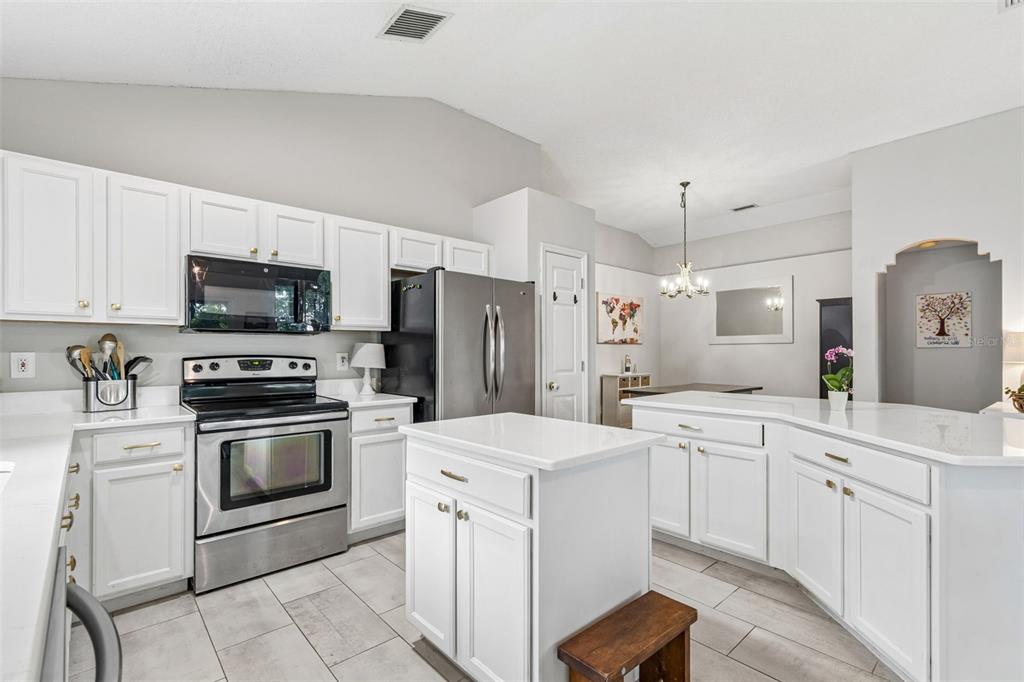 A kitchen features white cabinets, stainless steel appliances, a center island, and light-colored tile flooring — 6312 ASHFIELD PLACE, WESLEY CHAPEL, FL