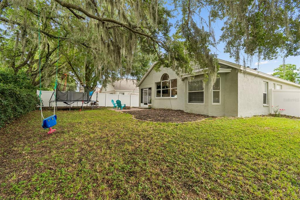 A backyard with a swing, a trampoline, a patio, and a single-story house exterior — 6312 ASHFIELD PLACE, WESLEY CHAPEL, FL
