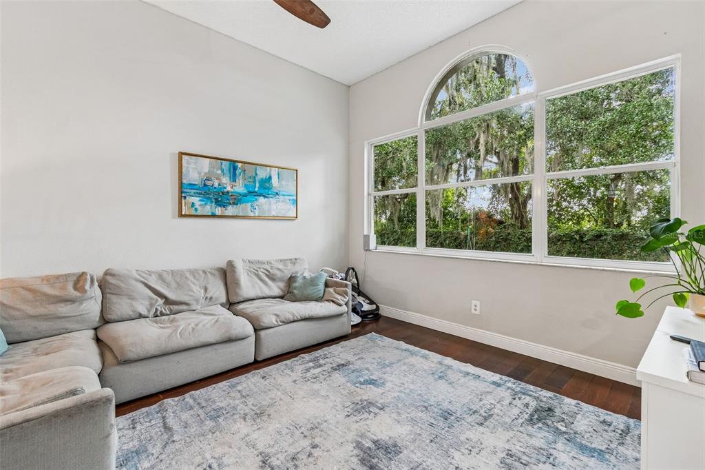A living room features a light gray sectional sofa, a blue abstract painting, and large windows — 6312 ASHFIELD PLACE, WESLEY CHAPEL, FL