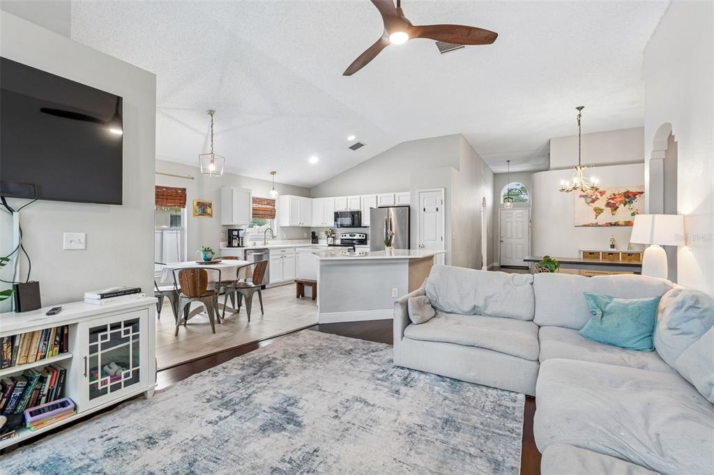 A living room with a sectional sofa opens into a kitchen with white cabinetry — 6312 ASHFIELD PLACE, WESLEY CHAPEL, FL