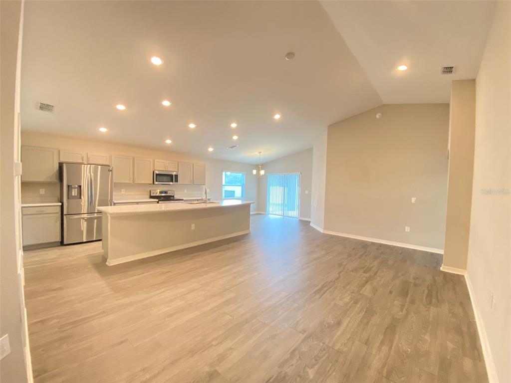 An open-concept kitchen and living area featuring light wood-look flooring and white cabinetry — 188 FOXTAIL LOOP, DAVENPORT, FL