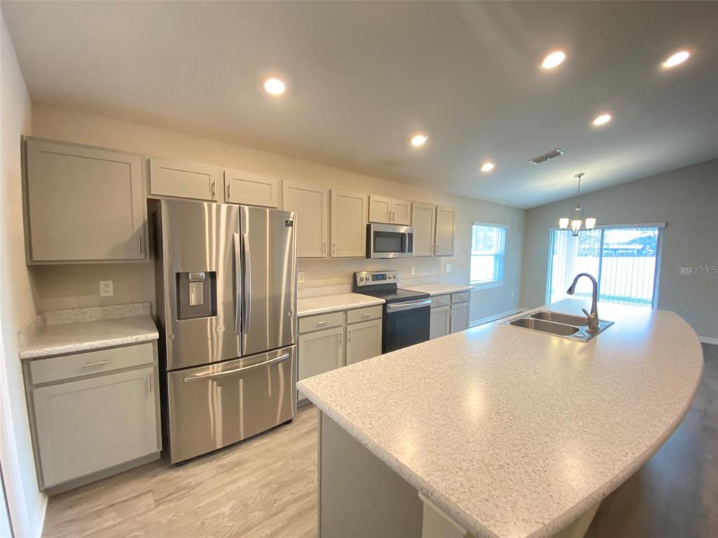 A kitchen features light gray cabinets, stainless steel appliances, and a large speckled island countertop — 188 FOXTAIL LOOP, DAVENPORT, FL