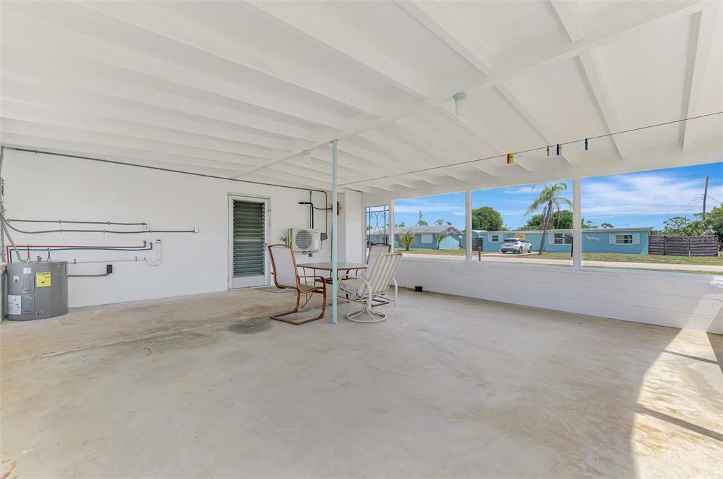 A covered concrete patio features a water heater, a small table with chairs, and screens — 2870 9TH STREET, ENGLEWOOD, FL