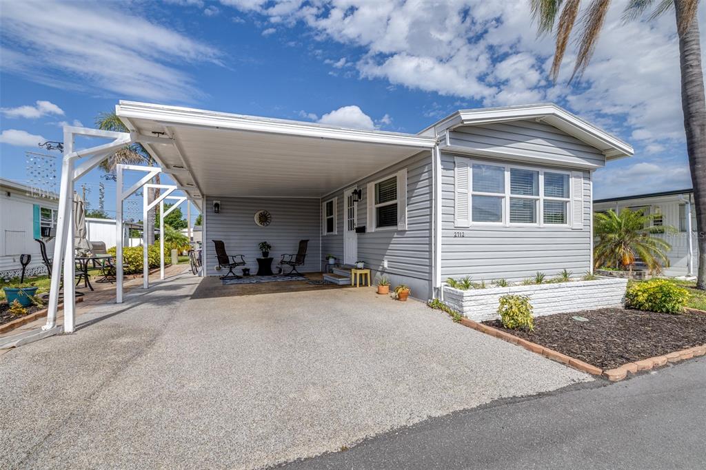 A light gray manufactured home features a large attached carport and a front patio area — 2712 17TH STREET LANE W, BRADENTON, FL