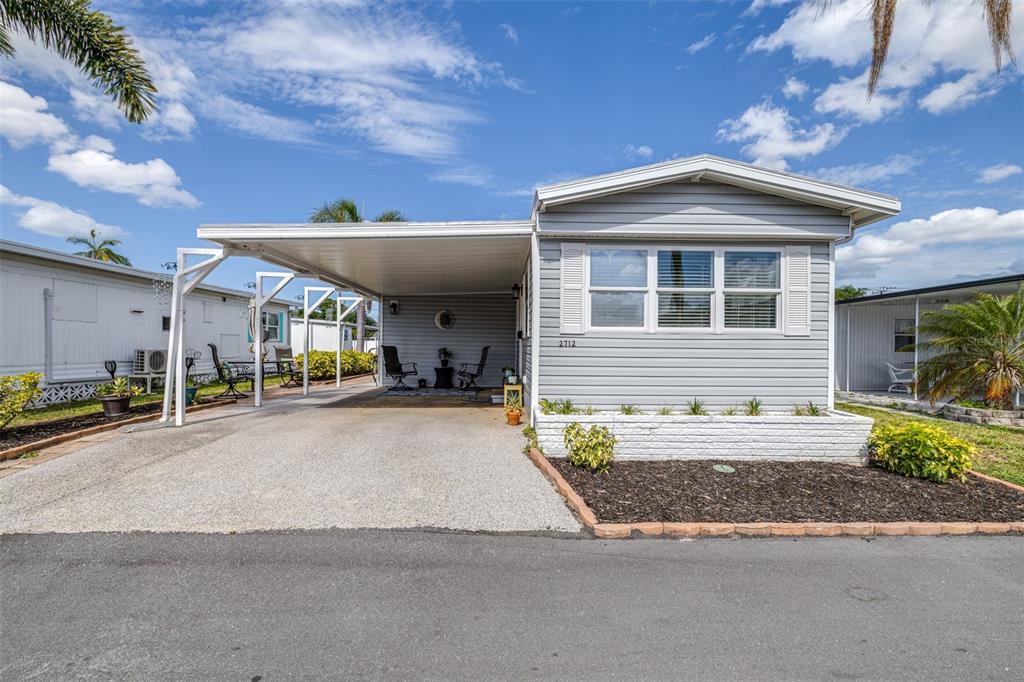 A light gray manufactured home features a large attached carport and a front garden bed — 2712 17TH STREET LANE W, BRADENTON, FL