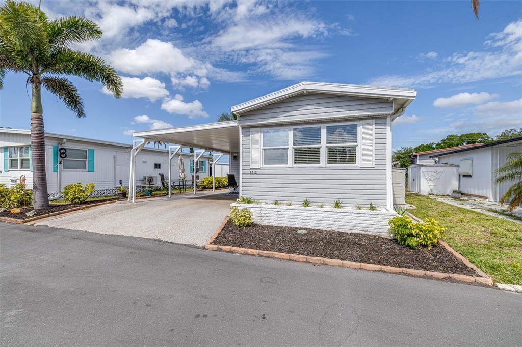 A light gray manufactured home features a carport, white shutters, and a front garden bed — 2712 17TH STREET LANE W, BRADENTON, FL