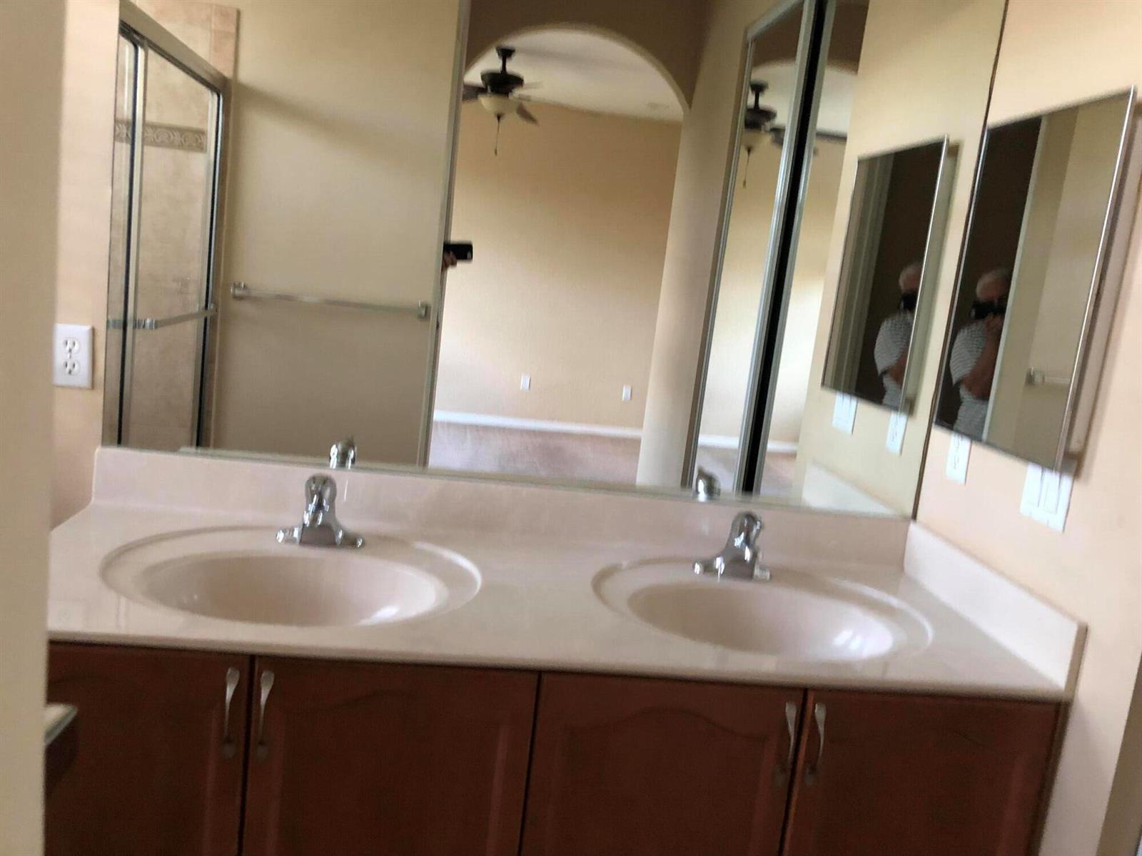 A bathroom features a double vanity with light-colored countertops and wood cabinets — 261 Lake Monterey Circle, Boynton Beach FL 33426, BOYNTON BEACH, FL