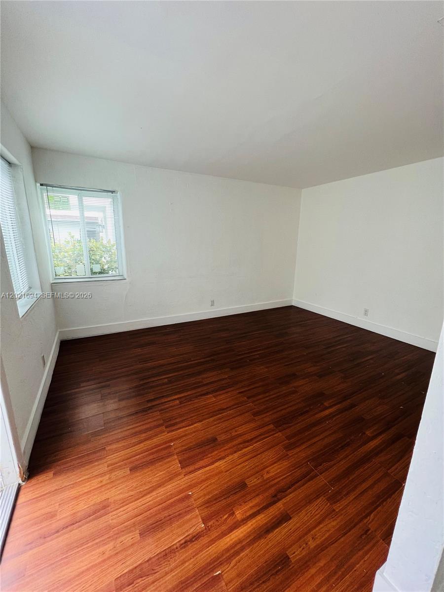 An empty room features white walls, dark wood-look flooring, and a window with blinds — 850 81st St # 3, Miami Beach FL 33141, MIAMI BEACH, FL