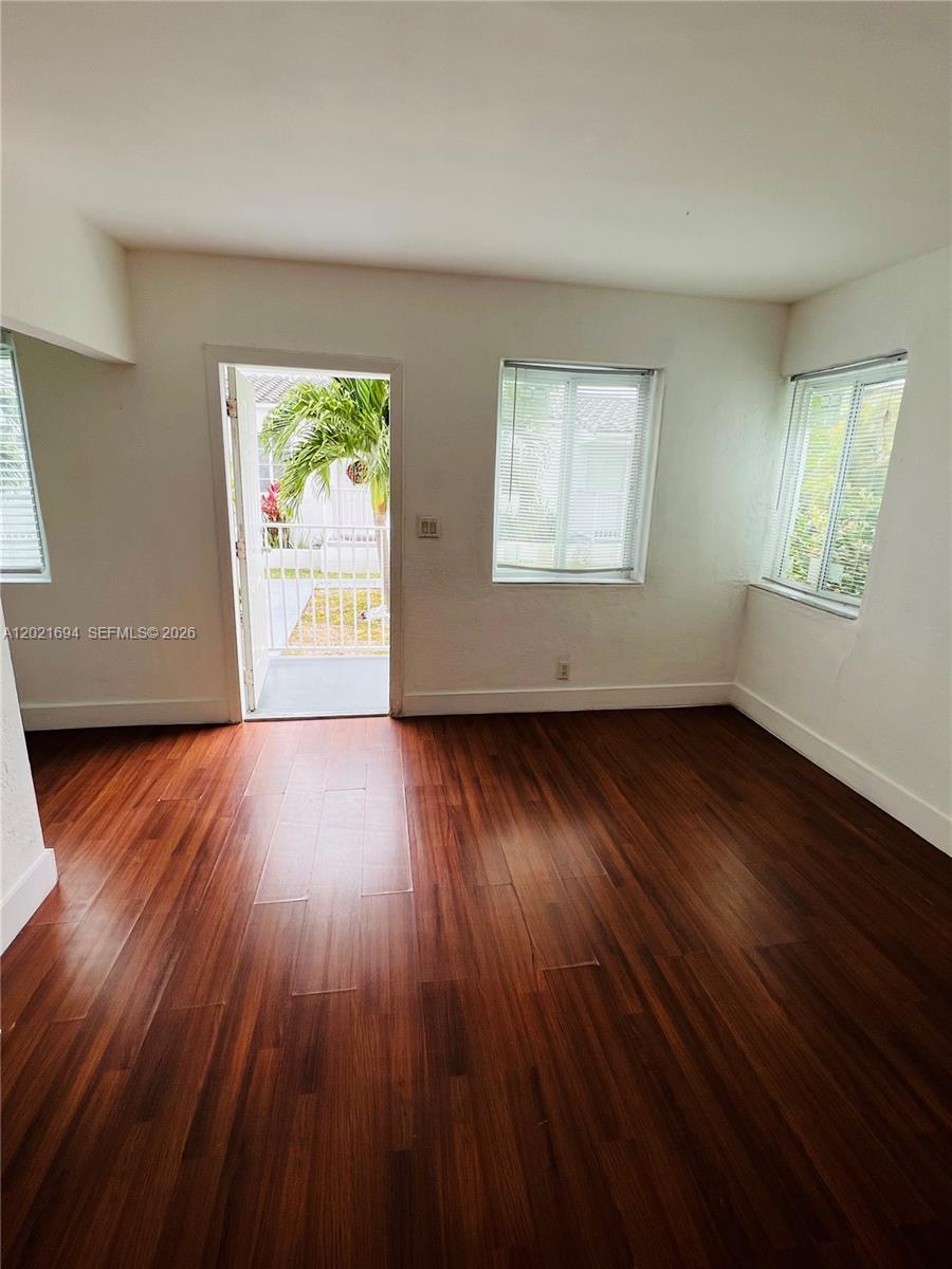 An empty room features dark wood-look flooring, white walls, and a door leading outside — 850 81st St # 3, Miami Beach FL 33141, MIAMI BEACH, FL