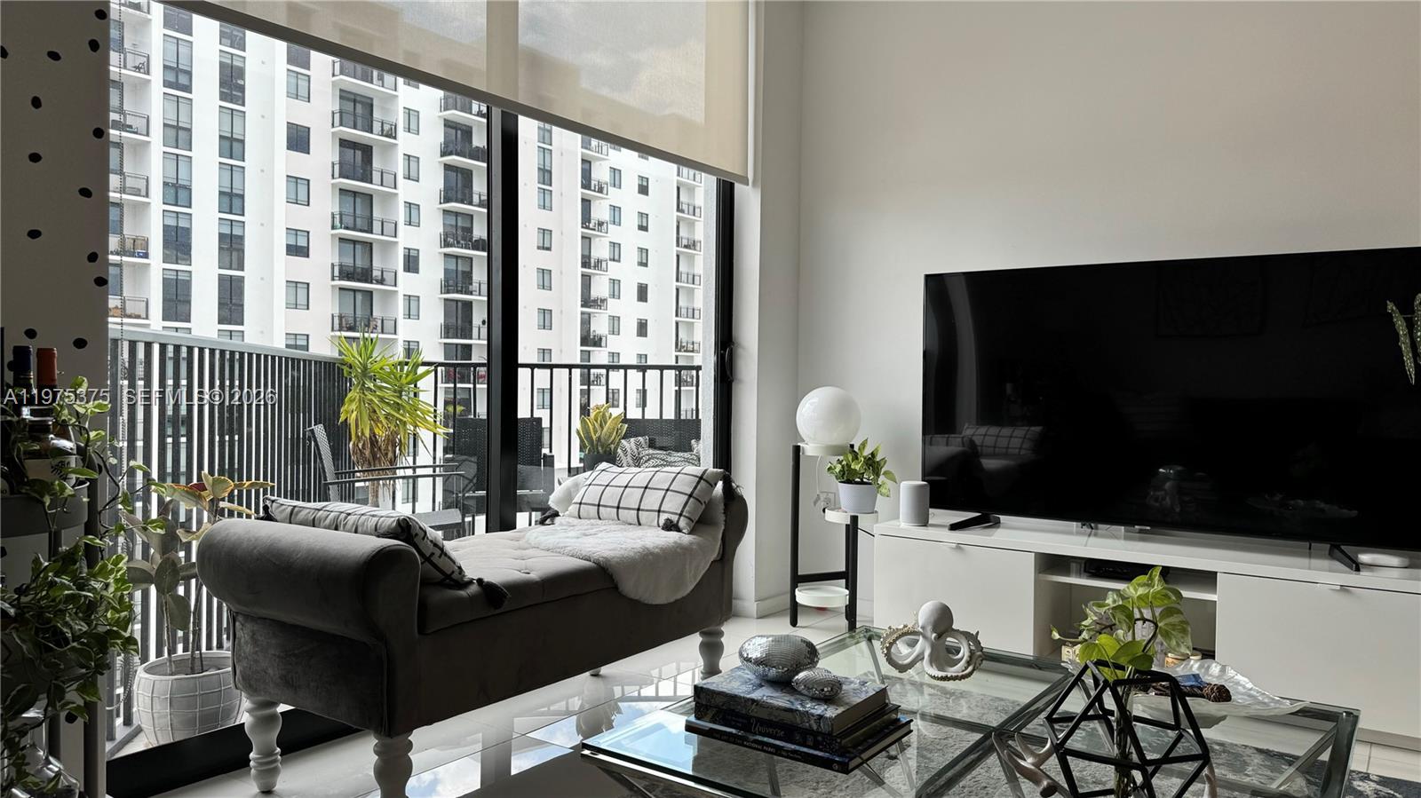 A modern living room features a grey chaise lounge, a glass coffee table, and a television — 5252 NW 85th Ave # 1203, Doral FL 33166, DORAL, FL