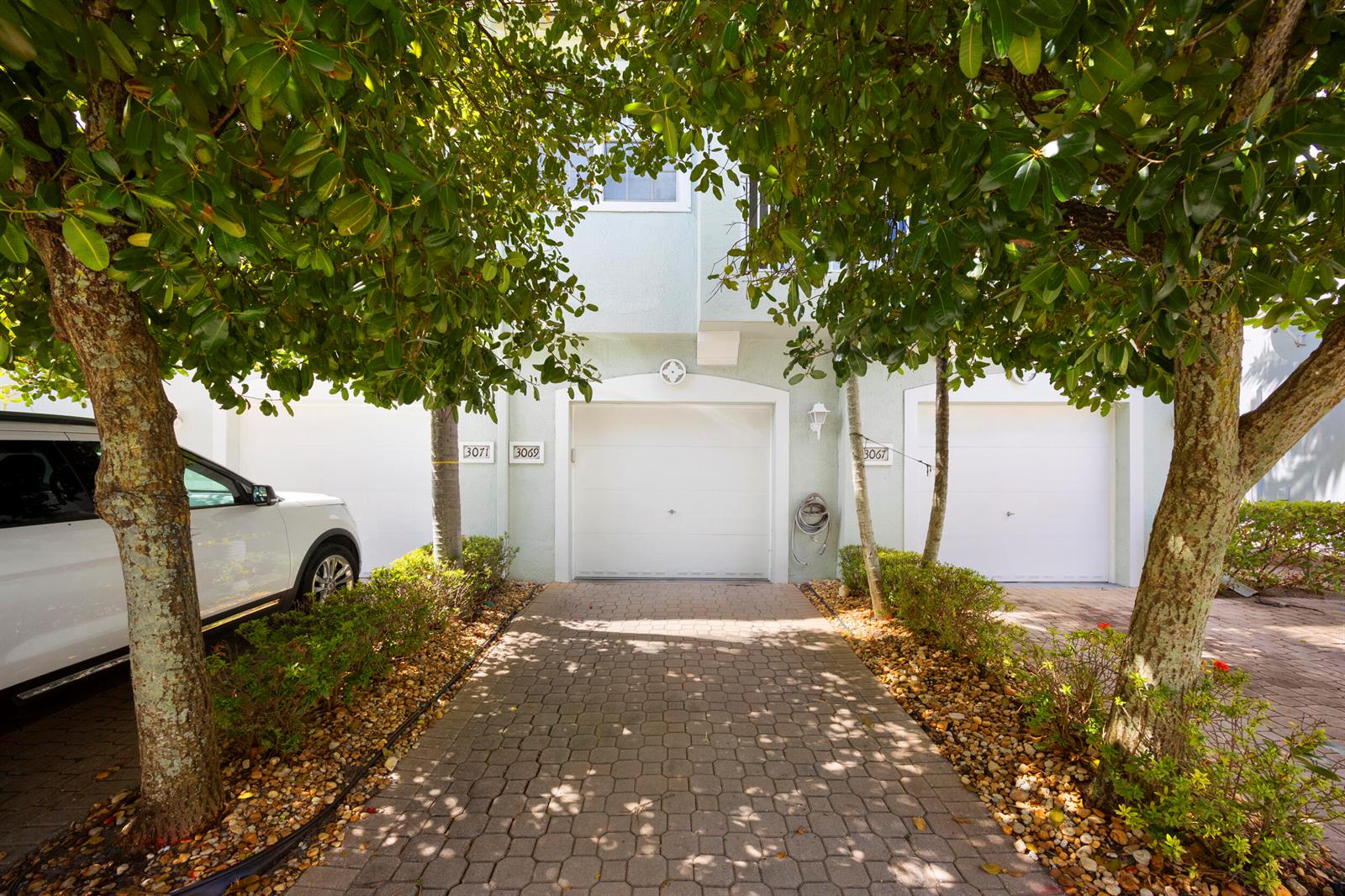 A paved driveway leads to three white garage doors on a light-colored building exterior — 3069 Laurel Ridge Circle, Riviera Beach FL 33404, RIVIERA BEACH, FL