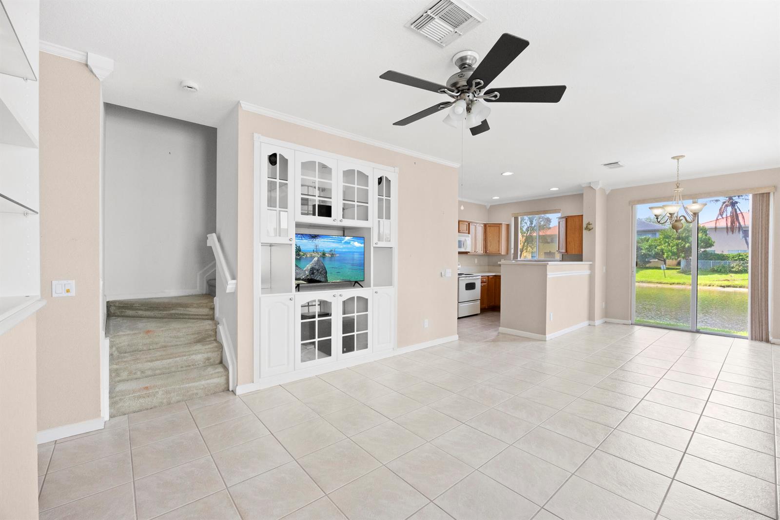 A living room with tile floors, a built-in media center, stairs, and a kitchen view — 3069 Laurel Ridge Circle, Riviera Beach FL 33404, RIVIERA BEACH, FL