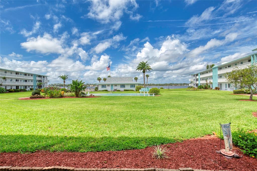 A grassy courtyard sits between two apartment buildings with a small clubhouse and water view — 3013 N HALIFAX AVENUE UNIT B3, DAYTONA BEACH, FL