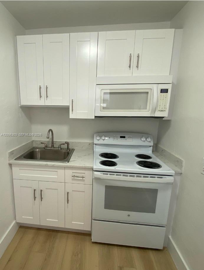 A small kitchen features white cabinets, a stainless steel sink, and a white electric range — 3669 Thomas Ave # 9, Miami FL 33133, MIAMI, FL