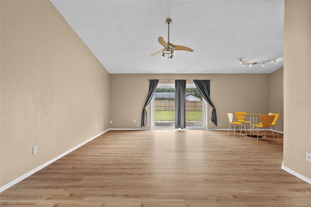A spacious living room with light wood-look flooring, a ceiling fan, and sliding glass doors — 8040 CLOVERGLEN CIRCLE, ORLANDO, FL