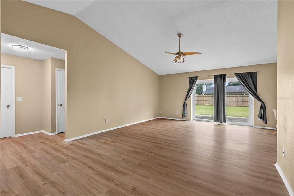 An empty living room features light wood-look flooring, a vaulted ceiling, and sliding glass doors — 8040 CLOVERGLEN CIRCLE, ORLANDO, FL