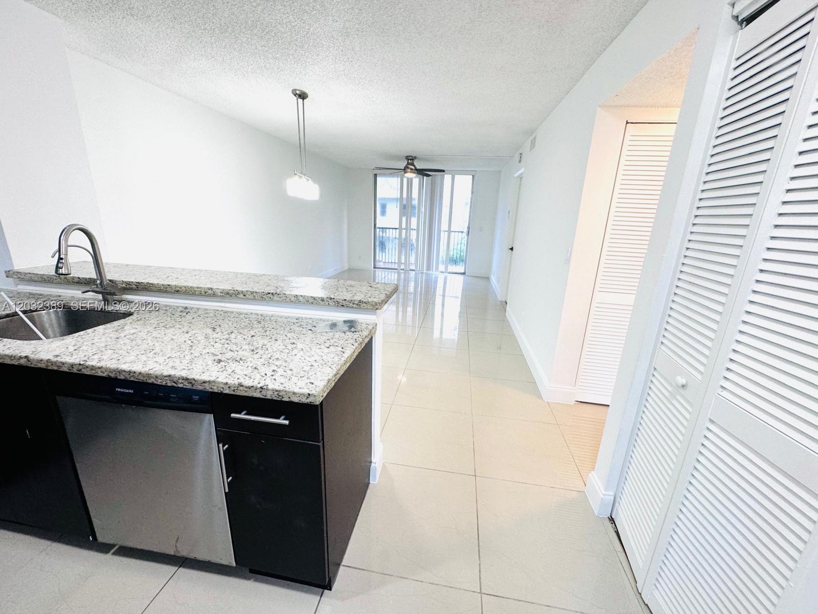 A kitchen with granite countertops and dark cabinets overlooks an open-concept living area — MIRAMAR, FL