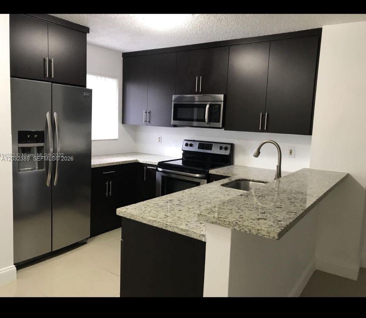 A kitchen features dark wood cabinets, stainless steel appliances, and a granite countertop peninsula — MIRAMAR, FL