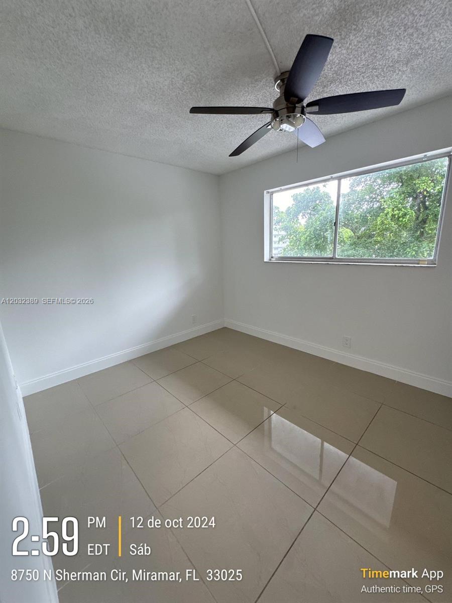 An empty room features light-colored tile flooring, white walls, and a ceiling fan — MIRAMAR, FL
