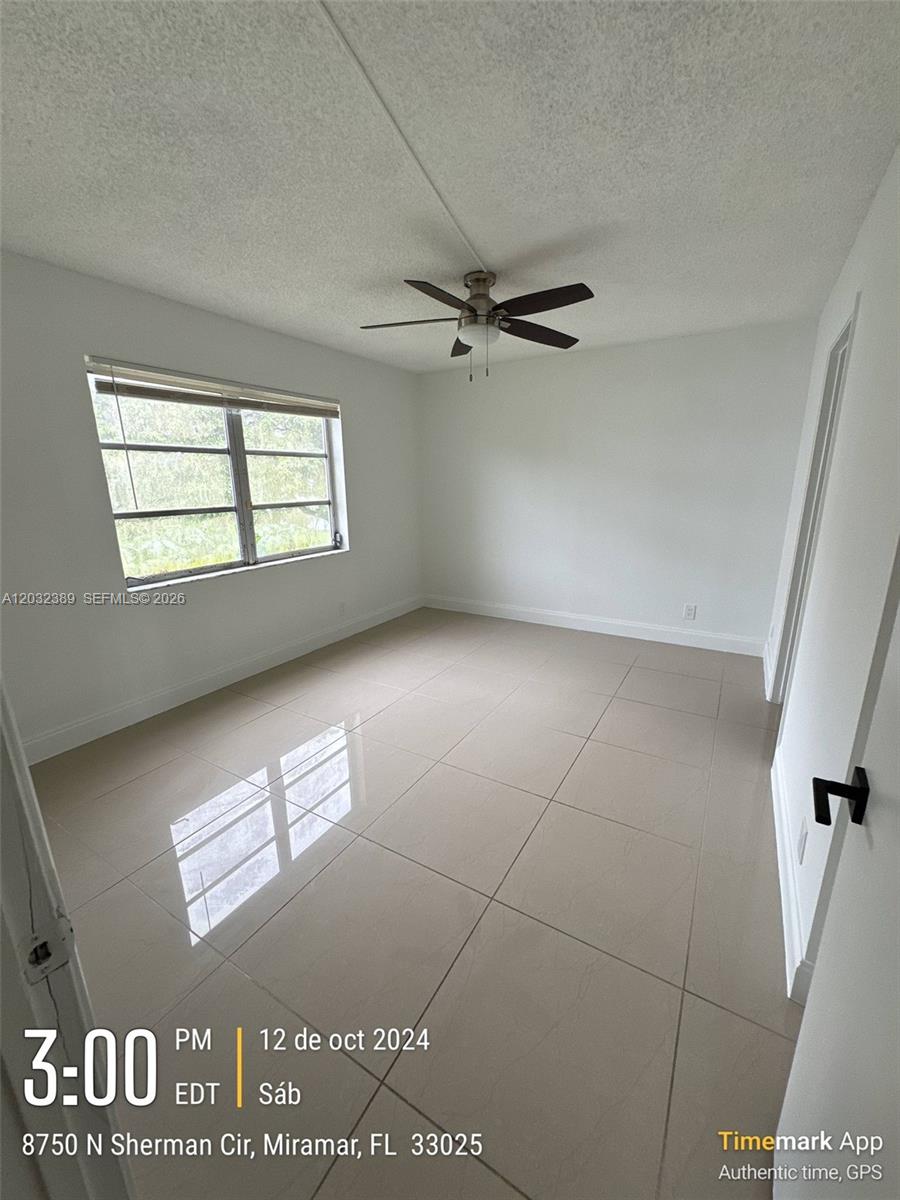 An empty bedroom features light-colored tile flooring, white walls, and a ceiling fan — MIRAMAR, FL