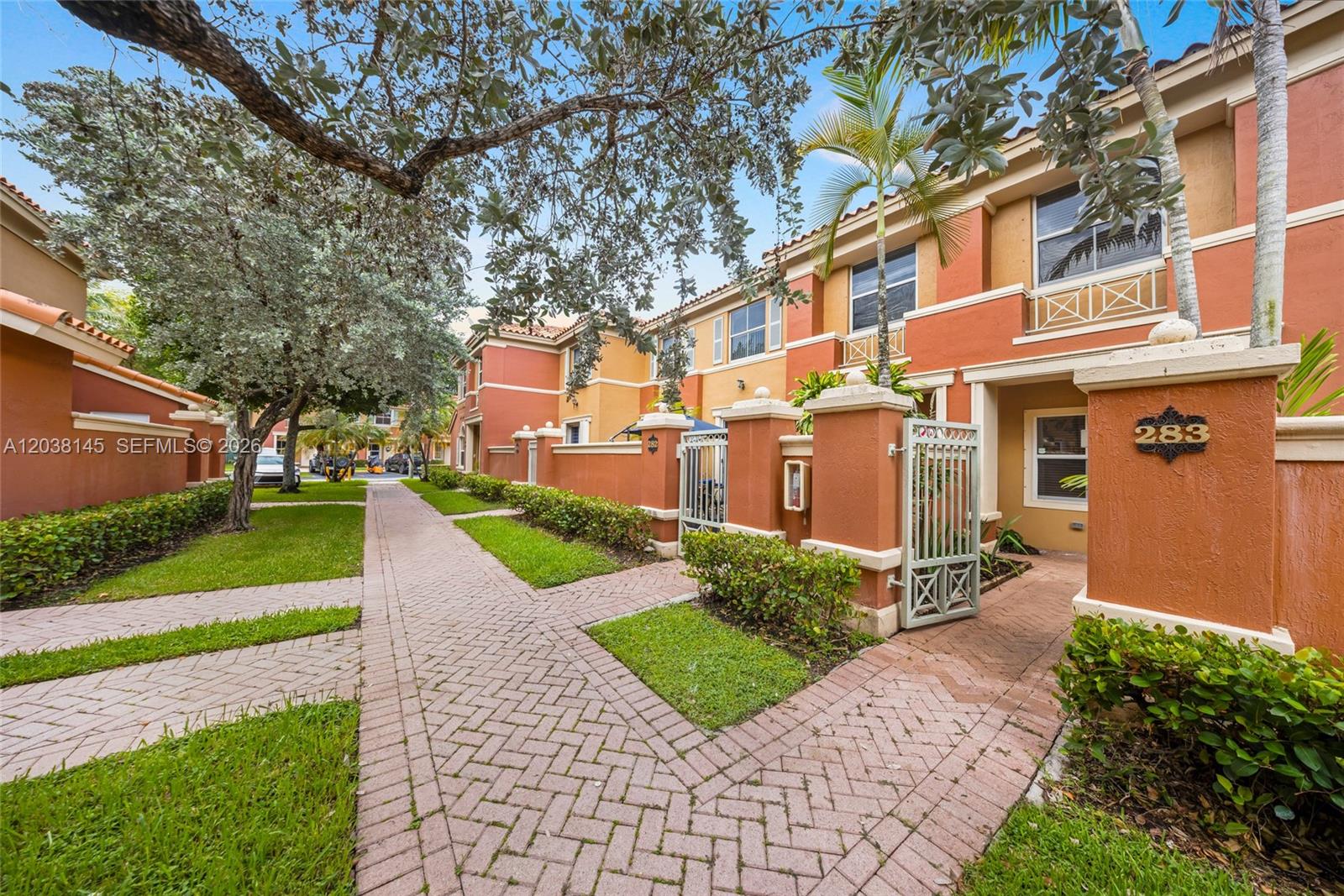 A paved walkway leads to the entrance of a multi-story townhouse with orange stucco walls — 11411 NW 60th St # 283, Doral FL 33178, DORAL, FL