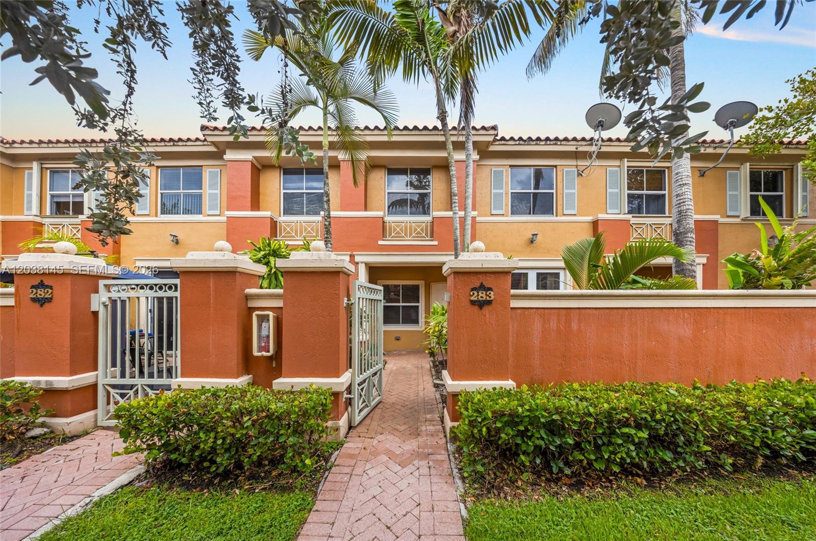 A two-story townhouse exterior features orange stucco walls, a brick walkway, and gated entrances — 11411 NW 60th St # 283, Doral FL 33178, DORAL, FL