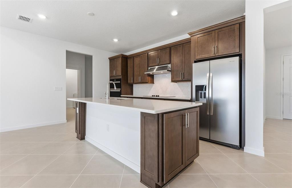 A modern kitchen features dark wood cabinets, a white quartz island, and stainless steel appliances — 6736 SW 89TH LANE, OCALA, FL