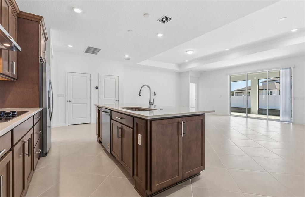 A kitchen with dark wood cabinets, a central island, and tile flooring leads to sliding doors — 6736 SW 89TH LANE, OCALA, FL