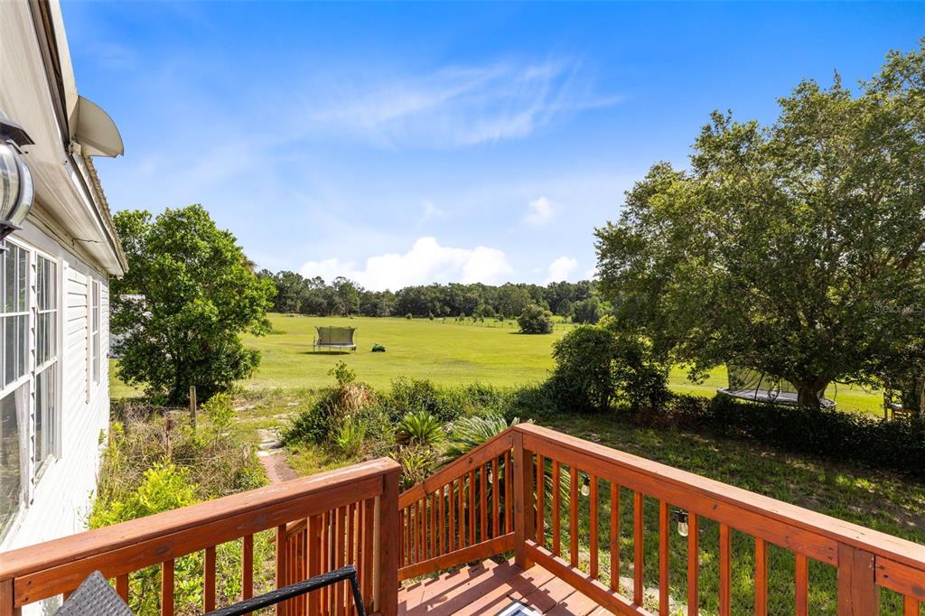 A wooden deck overlooks a large grassy backyard with trees and a distant trampoline — 35729 HUFF ROAD, EUSTIS, FL