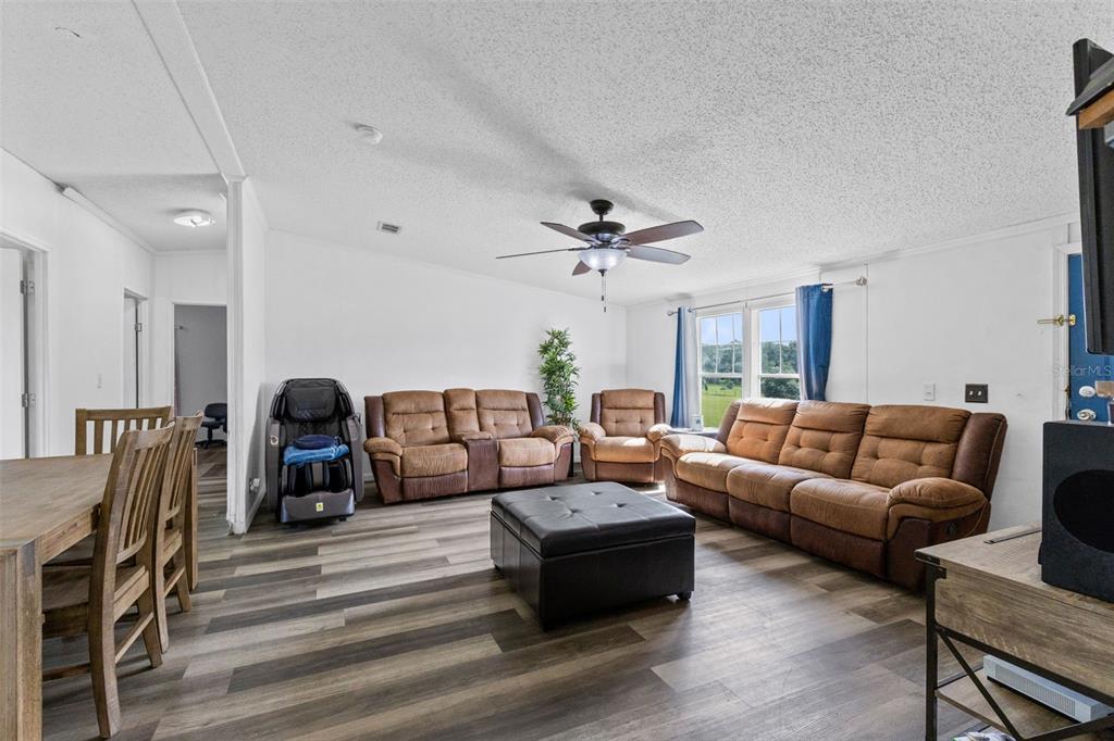 A living room features brown leather furniture, a black ottoman, and wood-look vinyl flooring — 35729 HUFF ROAD, EUSTIS, FL