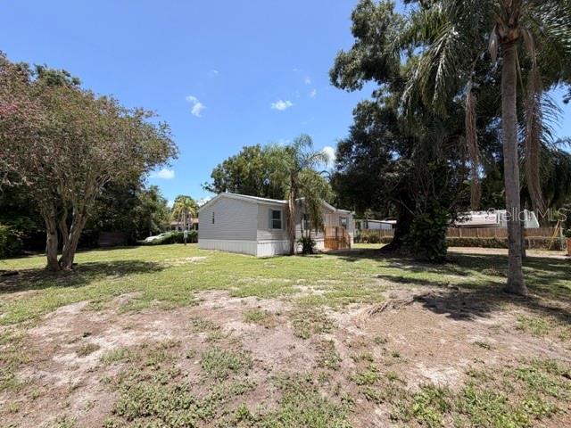 A light-colored mobile home sits on a grassy lot surrounded by trees and palms — 4301 SHERWICK DRIVE, TAMPA, FL