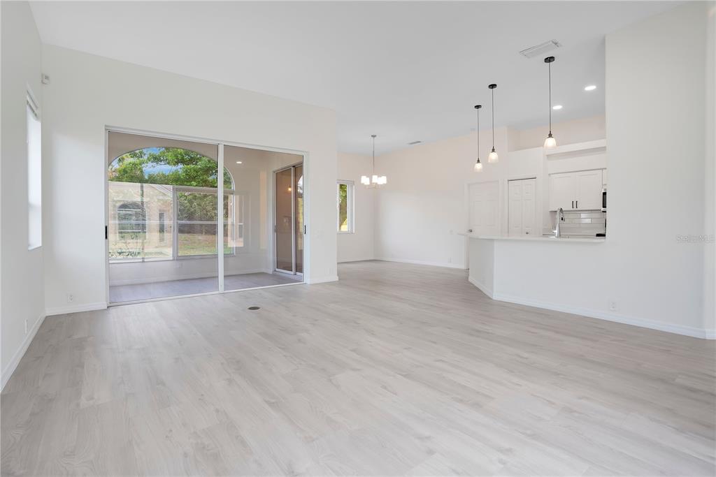 An open-concept living area features light wood-look flooring, a kitchen island, and sliding glass doors — 8533 GATEWAY COURT, ENGLEWOOD, FL