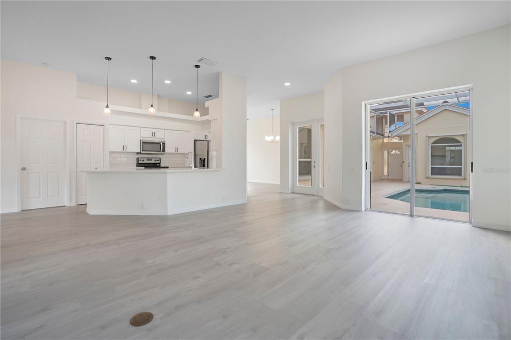 An open-concept kitchen and living area with light wood floors, white cabinetry, and pool access — 8533 GATEWAY COURT, ENGLEWOOD, FL