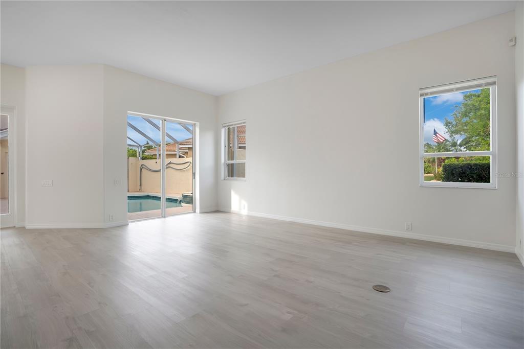 An empty room with light wood-look flooring, white walls, sliding glass doors, and a window — 8533 GATEWAY COURT, ENGLEWOOD, FL