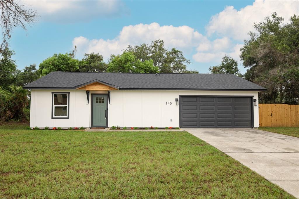 A single-story house with white siding, a dark roof, a green door, and a garage — 940 S DEAN CIRCLE, DELTONA, FL