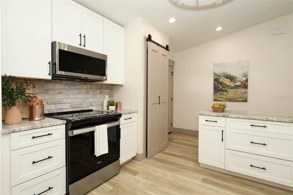 A kitchen features white cabinets, a brick backsplash, stainless steel appliances, and a sliding barn door — 940 S DEAN CIRCLE, DELTONA, FL