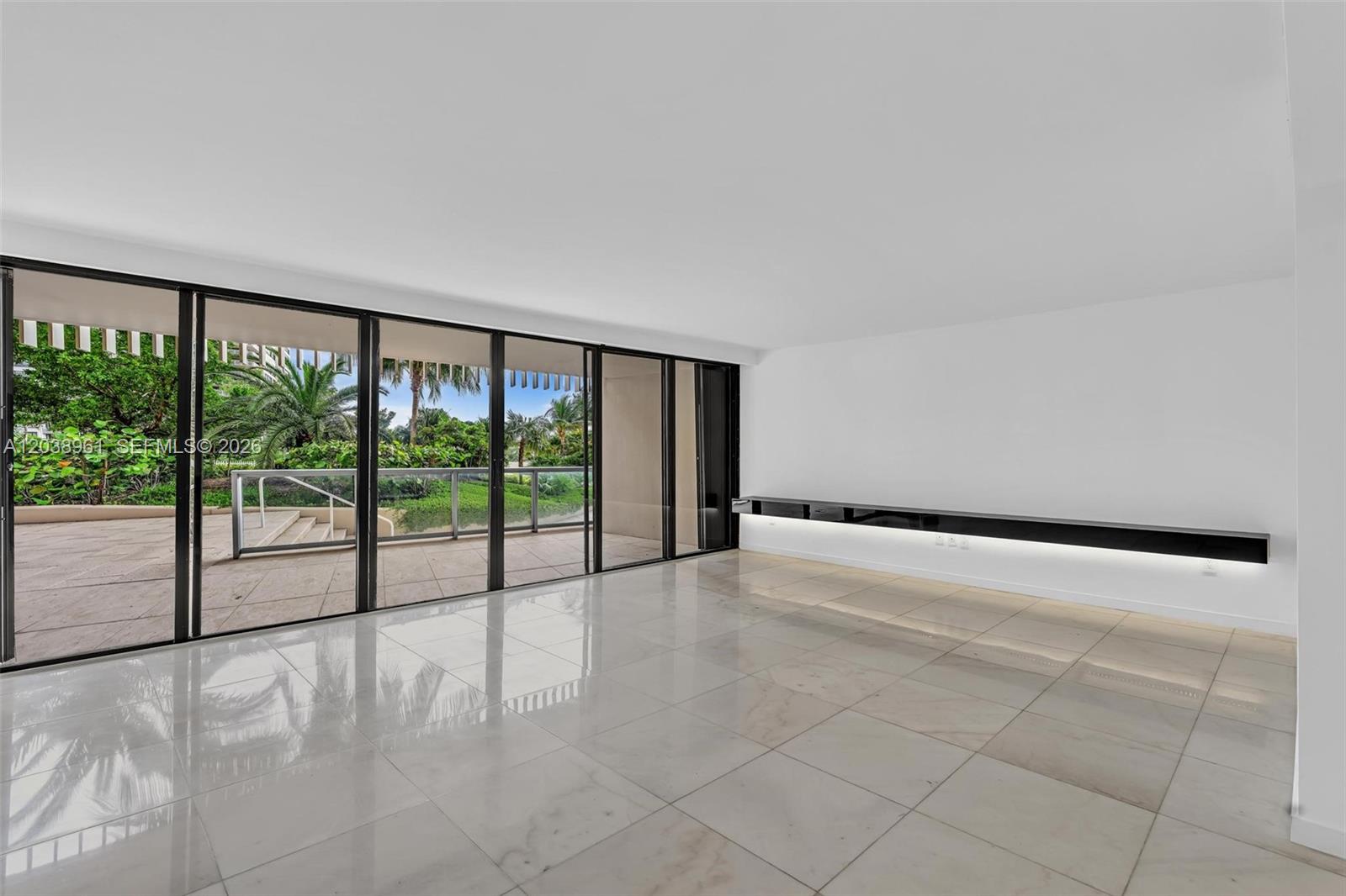 A bright, minimalist living room features large glass sliding doors, white walls, and tiled floors — 2 Grove Isle Dr # B205, Miami FL 33133, MIAMI, FL